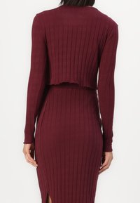 Burgunderfarbendes geripptes Kleid mit langen Ärmeln und kurzem Oberteil. Verfügt über eine elegante Textur und einen seitlichen Schlitz für zusätzliche Details.
