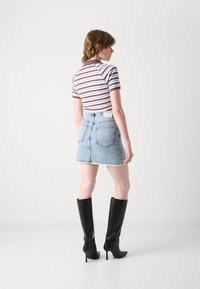 Prajčana majica s kratkimi rokavi v rjavi in beli barvi, v kombinaciji z svetlo modrim denim mini krilom z raztrganim robom in zadnjimi žepi. Črne škornje do kolen.