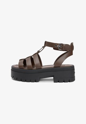 Brązowy skórzany sandał gladiator z grubą czarną podeszwą z głębokim bieżnikiem i regulowanym paskiem na kostkę z metalową klamrą.