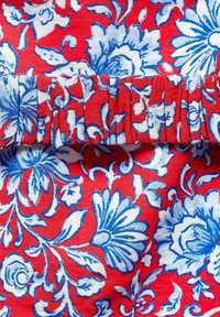 Rode stof met een bloemenpatroon in blauw en wit, met een geplooide, gerimpelde randafwerking. Textuur, katoenen materiaal.