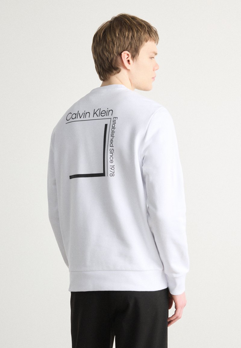 Sudadera blanca con un logotipo gráfico negro y texto en la parte posterior, con un diseño rectangular minimalista y puños y dobladillo acanalados.