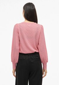 Maglione rosa con texture e maniche lunghe a sbuffo, caratterizzato da un collo rotondo e una vestibilità ampia, abbinato a pantaloni neri con vita elastica.