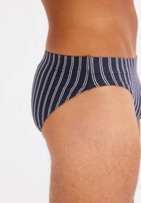 Slip da nuoto blu navy con strisce verticali bianche, caratterizzati da un design a vita bassa e una cintura elastica. Tessuto morbido al tatto.
