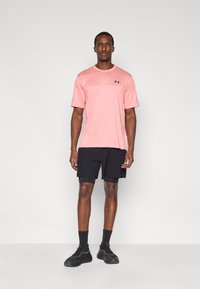 Ροζ αθλητική μπλούζα με κοντά μανίκια και υφασματικό σχέδιο, σετ με μαύρο σορτς και μαύρα αθλητικά παπούτσια.