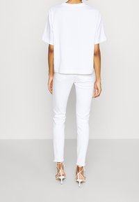 Camiseta de algodón blanca de gran tamaño, combinada con jeans blancos ajustados y tacones blancos con tiras. Textura suave, diseño minimalista, sin patrones.