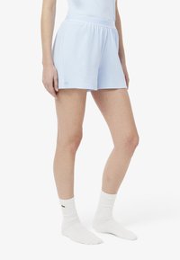 Pantalones cortos deportivos de color azul claro con una cinturilla elástica, textura suave y un pequeño detalle del logo en el lado izquierdo. Combinados con calcetines blancos de canalé.