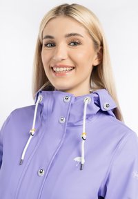 Jachetă impermeabilă lavandă cu guler înalt, șnururi albe și accesorii argintii. Are un logo alb cu umbrelă pe piept.