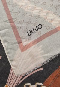 Sciarpa Liu Jo realizzata in tessuto leggero e decorato in tonalità pastello con accenti marroni e un bordo frangiato. Il logo del marchio è visibile.