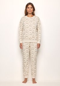 Conjunto de loungewear de color beige claro que incluye un sudadera de cuello redondo y pantalones tipo jogger. Ambas piezas están adornadas con un patrón repetido de caras de oso.