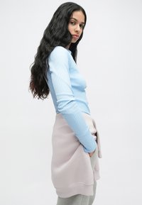 Ανοιχτό μπλε ριγωτό τοπ με μακριά μανίκια συνδυασμένο με μια ανοιχτό ροζ φούστα τύπου περιτυλίγματος πάνω από γκρι αθλητικά παντελόνια. Η υφή φαίνεται απαλή και casual.