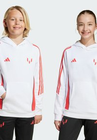 Sweatshirt à capuche blanche avec des rayures rouges sur les manches, poches avant et logo. Pantalons noirs avec des accents rouges. Tissu lisse et coupe décontractée.