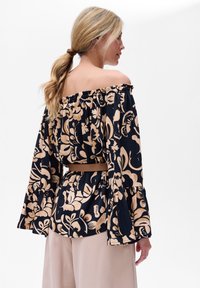 Bluzka typu off-the-shoulder w kolorze granatowym z beżowym wzorem kwiatowym; rozszerzane rękawy i falbaniasty dół; zestawiona z beżowymi spodniami.