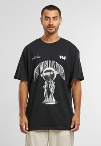 T-shirt noir en coton avec un imprimé graphique d'un globe et de figures, portant le texte "LE MONDE EST À VOUS" en lettres blanches en gras.