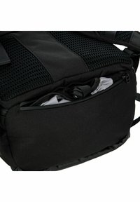 Bolsa de tela negra con un panel de malla, que cuenta con un bolsillo delantero con cremallera y correas ajustables. Textura suave y diseño resistente.