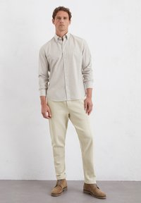 Helles grau gestreiftes Hemd mit Knopfleiste, beiger Jogginghose und braunen Wildlederstiefeln. Das Hemd hat einen Kragen und lange Ärmel.