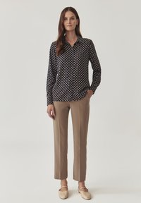 Camicia button-up blu navy con un piccolo motivo bianco, abbinata a pantaloni beige a gamba dritta e scarpe slip-on di colore chiaro.