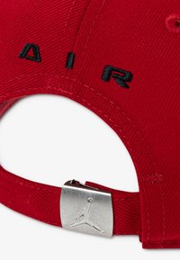 Κόκκινο καπέλο με κεντημένο μαύρο "AIR" στο μπροστινό μέρος, με μεταλλικό ασημί κούμπωμα ρύθμισης με το λογότυπο Jumpman. Υφασμάτινη υφή.