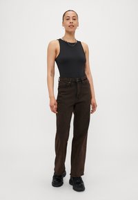 Svart ermeløs bodysuit kombinert med høy midje, rett ben, mørkebrune jeans. Modellen har på seg svarte, kraftige sko med en kjedehalskjede.