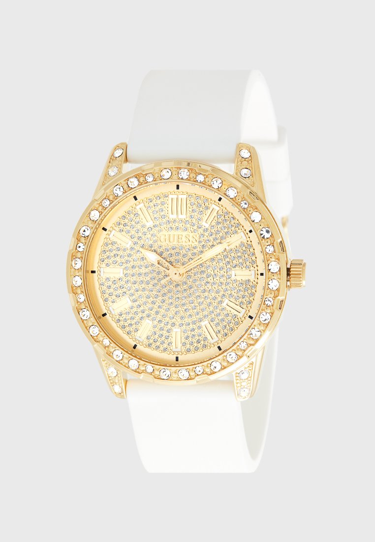 Montre dorée avec un cadran incrusté de cristaux scintillants, un bracelet en silicone blanc et des accents en métal doré. Présente des chiffres romains et une finition brillante.