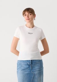 Bílý tričko s krátkým rukávem a kulatým výstřihem s potiskem "TOMMY JEANS New York" v černé barvě přes prsa, nošeno s džínovou sukní.