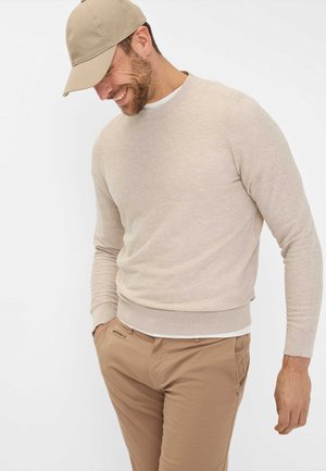 Beige sweater with a textured knit, crew neckline, and ribbed cuffs. Paired with light brown pants and a matching cap.