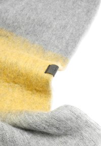 Woolny szal w gradientowych odcieniach szarości i żółci z miękkim, teksturowanym wykończeniem. Zawiera ciemną skórzaną metkę.