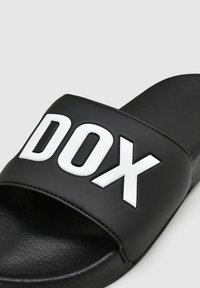 Zwarte schuimsandaal met een gestructureerde band en witte "DOX" letters. De voetbed is plat en glad, gemaakt van synthetisch materiaal.