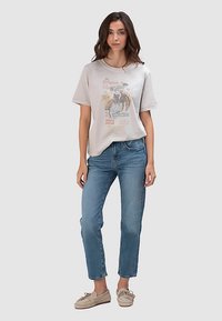 Lichtgrijs grafisch T-shirt met korte mouwen, voorzien van een print in vintage stijl. Gecombineerd met blauw hoogwaardige denim jeans en beige schoenen.