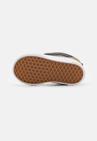 Suela de zapatilla con una superficie de goma texturizada; cuenta con una entresuela blanca y un patrón hexagonal marrón. Acentos en negro y dorado en la parte superior.