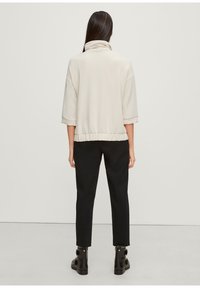 Lys beige fleece pullover med høj krave, trekvartærmer og en samlet kant, parret med sorte slim-fit bukser og ankelstøvler.