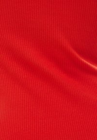 Tissu rouge à nervures avec une texture lisse, présentant des rayures verticales. Le matériau semble élastique et léger.