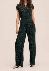 Zelený overal s puntíky vyrobený z lehké tkaniny, s páskem v pase, krátkými rukávy a širokými nohavicemi. Obsahuje knoflíkové zapínání vpředu.