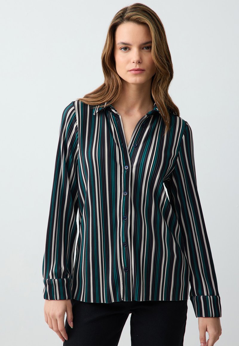 Koszula zapinana na guziki z pionowymi paskami w kolorze teal, czarnym i kremowym. Długie rękawy z guziczkami oraz kołnierz. Gładka struktura materiału.