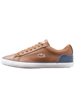 Brun læder sneaker med brune snørebånd, hvid sål, blå hæl accent og broderet krokodillelogo på siden.