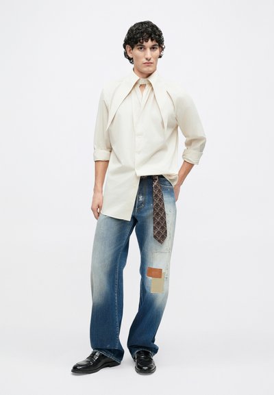 Light-colored button-up shirt with unique collar, paired with distressed denim jeans featuring patches and a patterned tie as an accent.