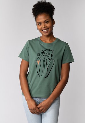 Groene katoenen T-shirt met een lijntekening van handen en een gezicht met een bloem, accentueert door een perzikkleurig hart. Korte mouwen, relaxed fit.