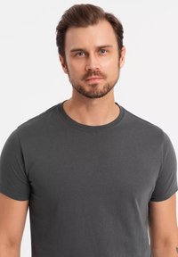 Tummanharmaa puuvillapaita, jossa on pyöreä kaula-aukko ja lyhyet hihat. Sujuva pinta, tyköistuva malli, ei näkyviä kuvioita tai graafisia elementtejä.