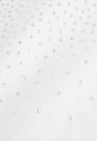 Valkoinen kangas, jossa on pehmeä tekstuuri ja joka on koristeltu pienillä, pyöreillä, kiiltävillä paljeteilla, jotka on aseteltu hajanaiseksi kuvioiksi.