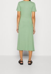 Minttu vihreä polvipituinen mekko, jossa on lyhyet hihat ja istuva vartalonmyötäinen yläosa. Mekon pinta on sileä ja muotoilu yksinkertainen ilman koristeita.