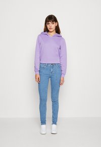 Haut à capuche lilas avec une poche kangourou, associé à un jean ajusté bleu clair et des baskets blanches. Le tissu semble doux et décontracté.