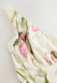 Material alb texturat cu model floral în roz și verde, prezentând o piesă vestimentară fără mâneci, cu cusături adunate lângă decolteu.