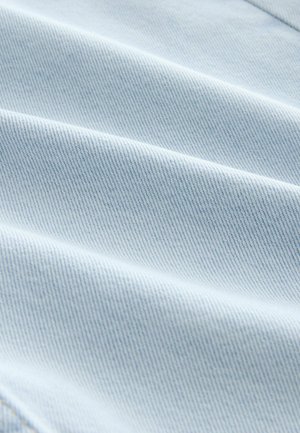 Šviesiai mėlynas džinsinis audinys su lygiu paviršiumi ir aiškiu šviesiniu raštu, demonstruojantis sulankstytas raukšles ir švelnų, lankstų išvaizdą.