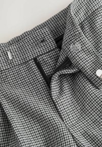 Materiał w szaro-czarny wzór houndstooth z paskiem w talii, zamkiem błyskawicznym i zapięciem na guzik. Oferuje gładką fakturę i szczegóły dopasowanego kroju.