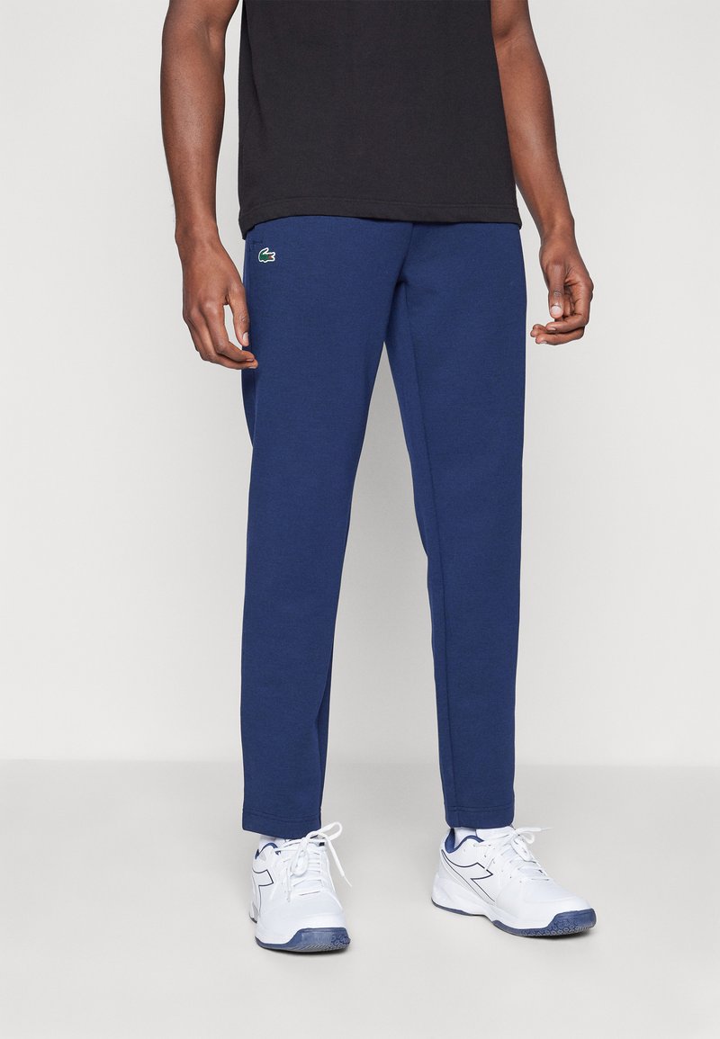 Mørkeblå joggebukser laget av bomullsmiksen, med en tettsittende design og elastisk midje, med en liten grønn logo på øvre lår.