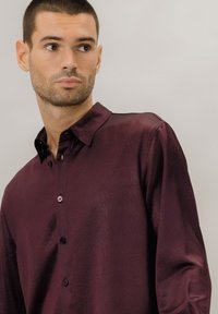 Vinrød skjorte med knapper foran, blank tekstur, lange ermer og klassisk krage. Har synlige knapper og en løs passform.