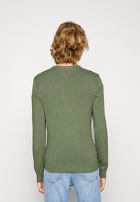 Olijfgroene lange mouwen gebreide trui met een ronde hals, geribde manchetten en onderkant. Zachte textuur met een slim fit, gecombineerd met lichtblauwe jeans.