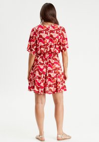 Short-sleeve, knee-length dress in red with abstract pink and burgundy patterns, cinched at the waist with a matching belt. Smooth fabric.