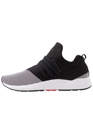 Sort-hvid atletiksneaker med strikket tå, tyk hvid sål, sorte snørebånd krydsende over midtfoden og trække-flig ved hælen.