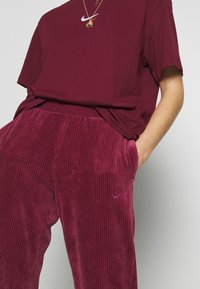 T-shirt en coton marron avec logo Nike et pantalon en velours côtelé marron avec des rayures verticales et un petit logo Nike brodé.