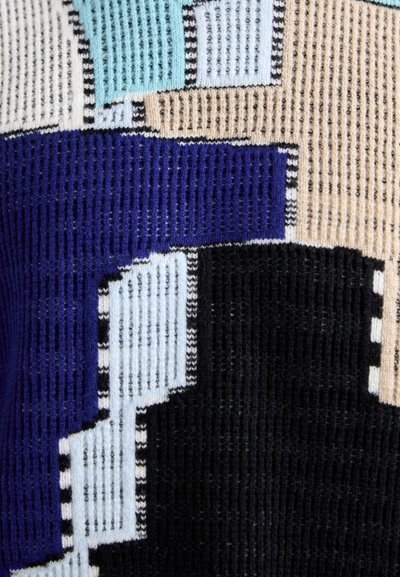 Tissu tricoté multicolore présentant des motifs géométriques en bleu, beige et noir. La texture est côtelée avec des sections distinctes.
